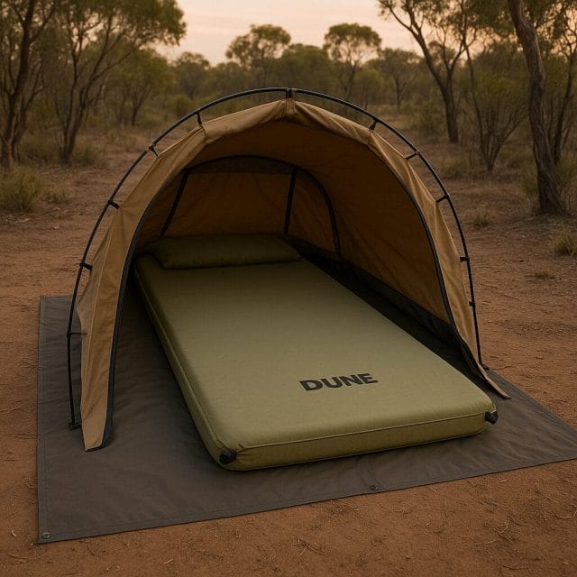 A wide angle photo of a Dune branded single self inflating camping mattress laid out inside a canvas swag at a bush campsite, with both twist valves visible near the head end, soft evening light, and a neat groundsheet under the swag to show proper setup.